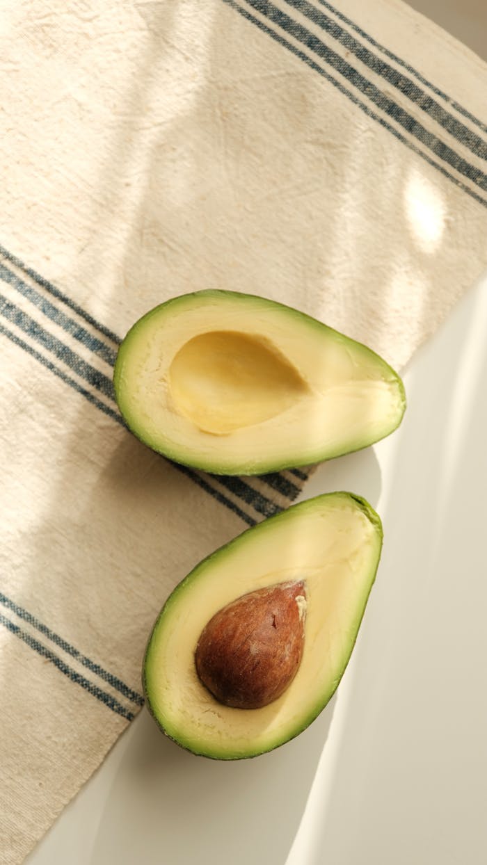 Top view of ripe avocado halves on striped kitchen cloth with natural lighting.