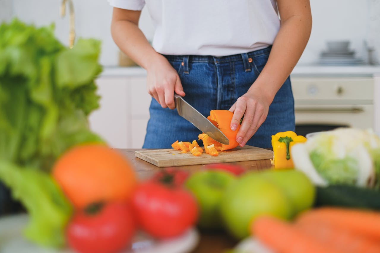 Woman chopping bell peppers on a cutting board surrounded by fresh vegetables.